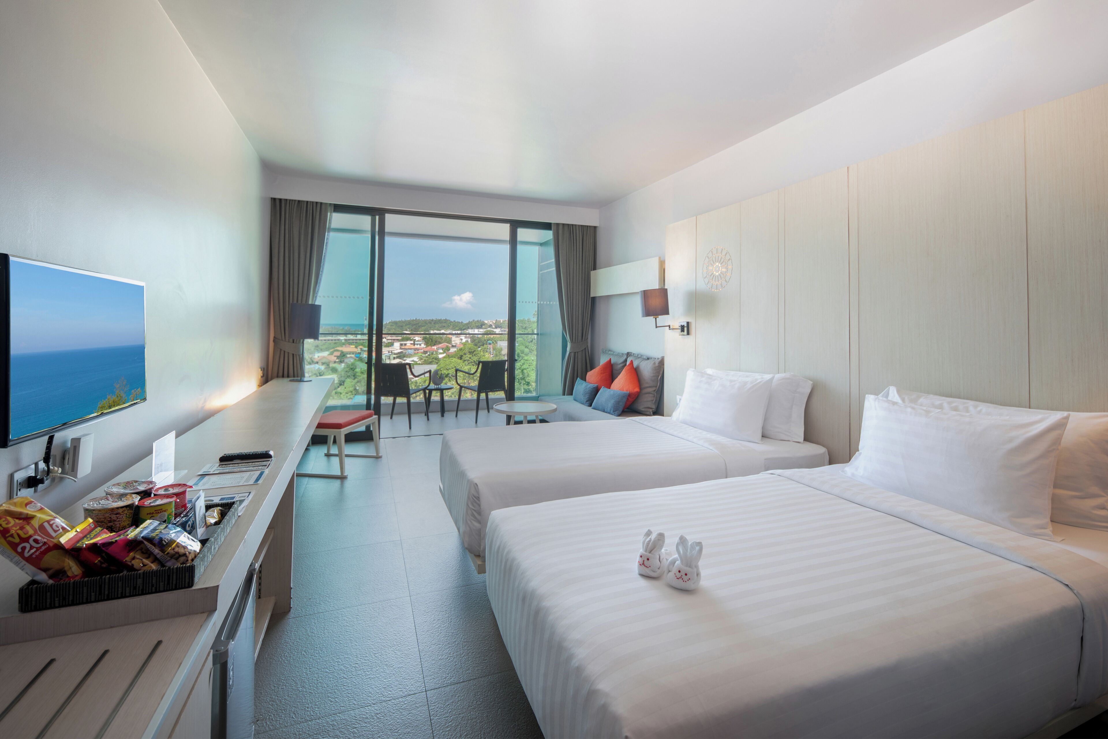 A hotel room with two beds, a desk, a TV, and a balcony with a view.