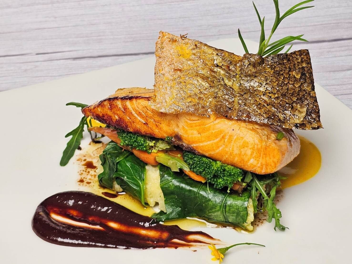 A dish with salmon, vegetables, and a sauce on a white plate.
