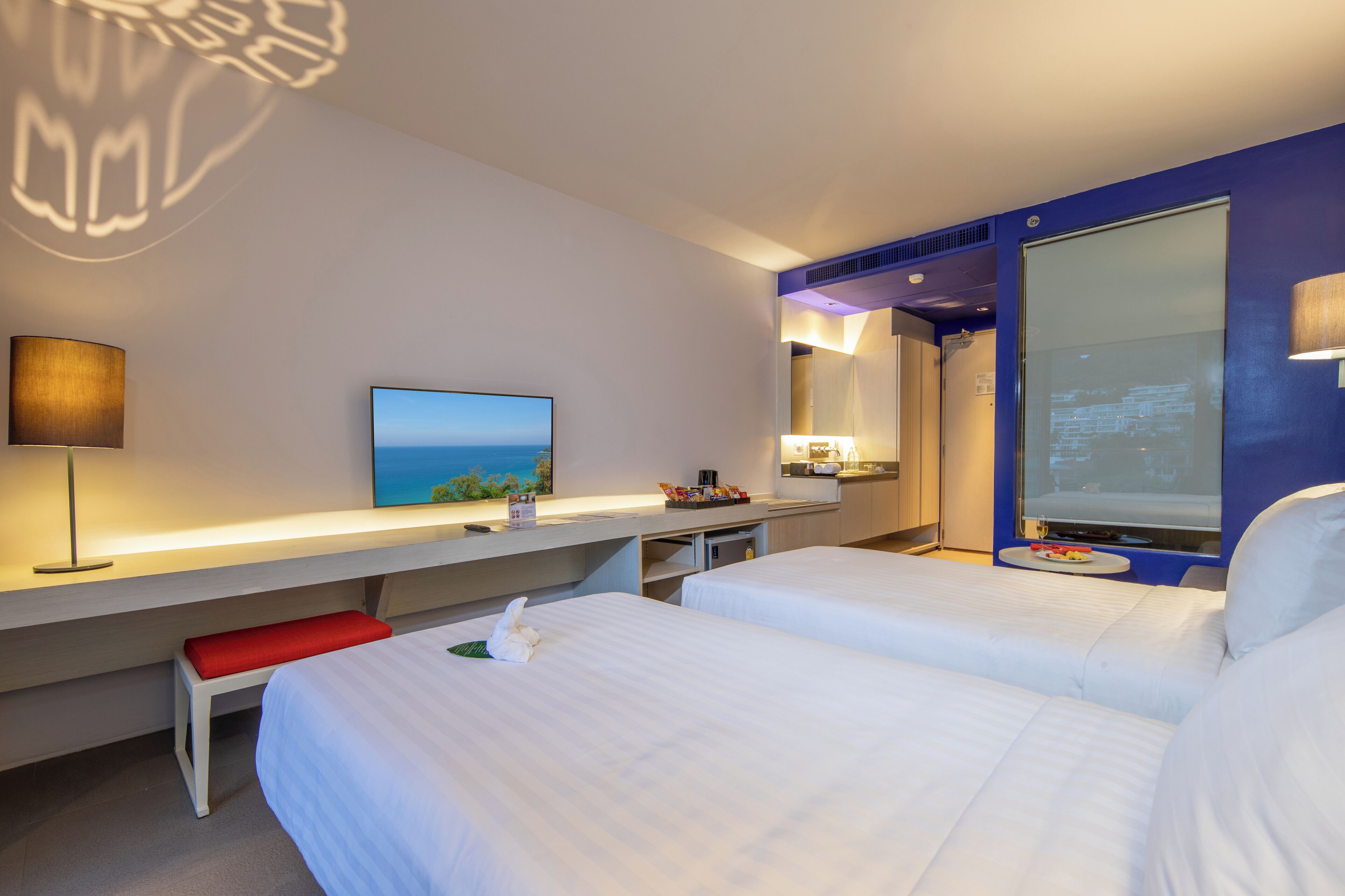 A hotel room with two beds, a desk, a TV, and a large window.