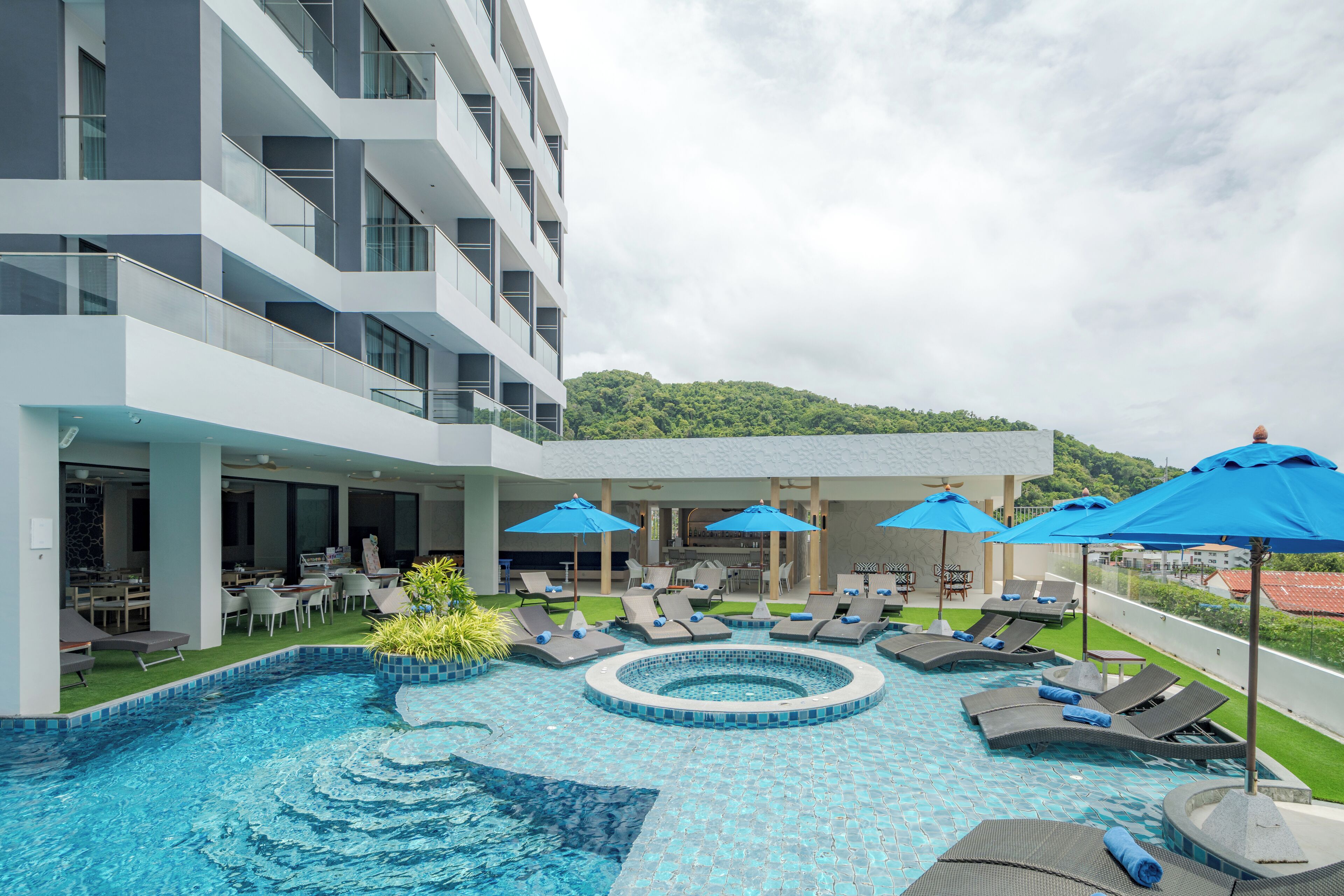 A modern hotel with a rooftop pool area, lounge chairs, and umbrellas.