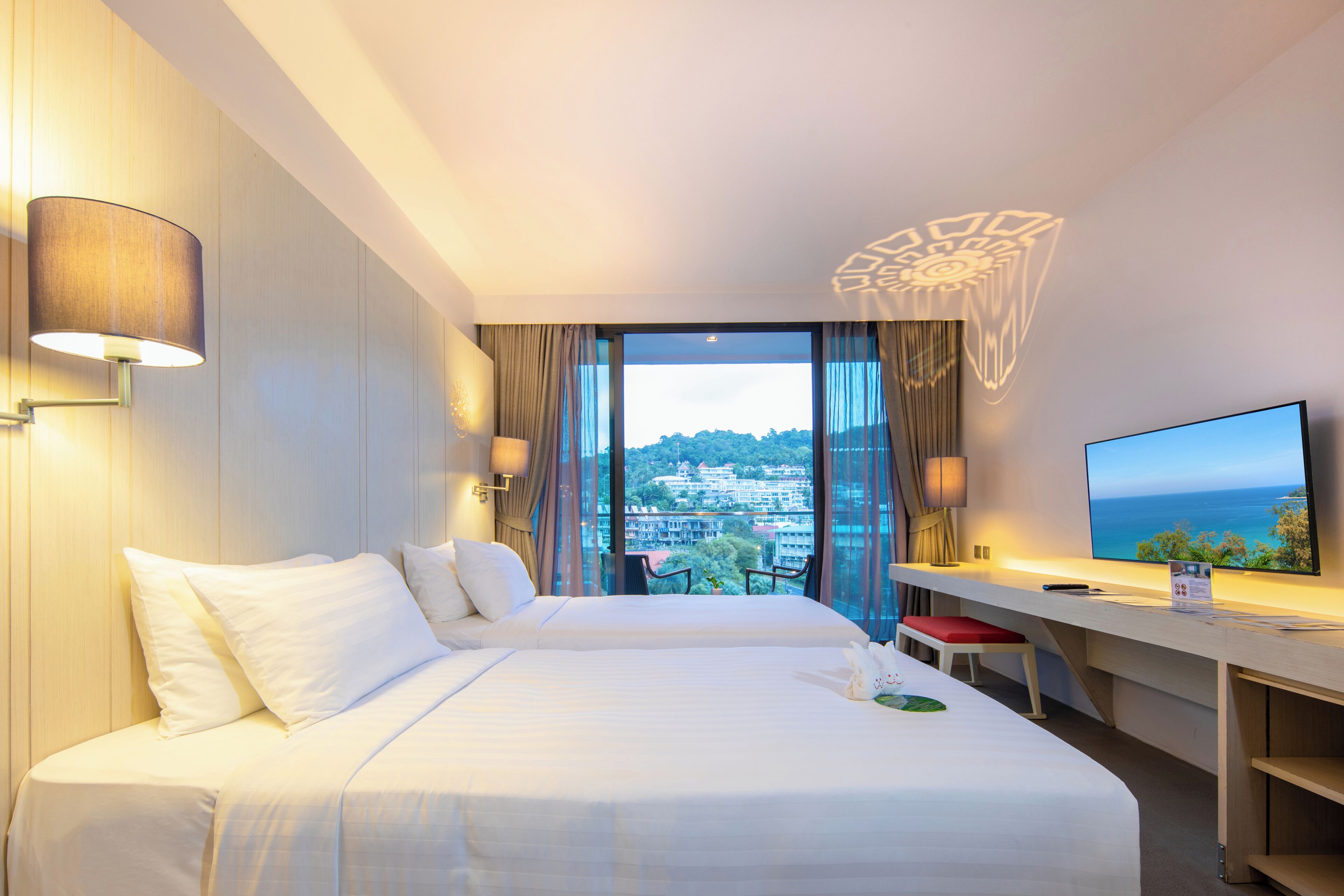 A hotel room with a bed, a desk, a TV, and a view of the city.