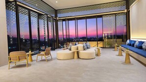 Un área de descanso moderna con un amplio ventanal que ofrece vistas a la ciudad al atardecer.