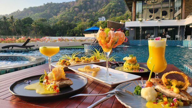 Una mesa de comedor con varios platos y bebidas junto a una piscina, con vistas a un paisaje montañoso.