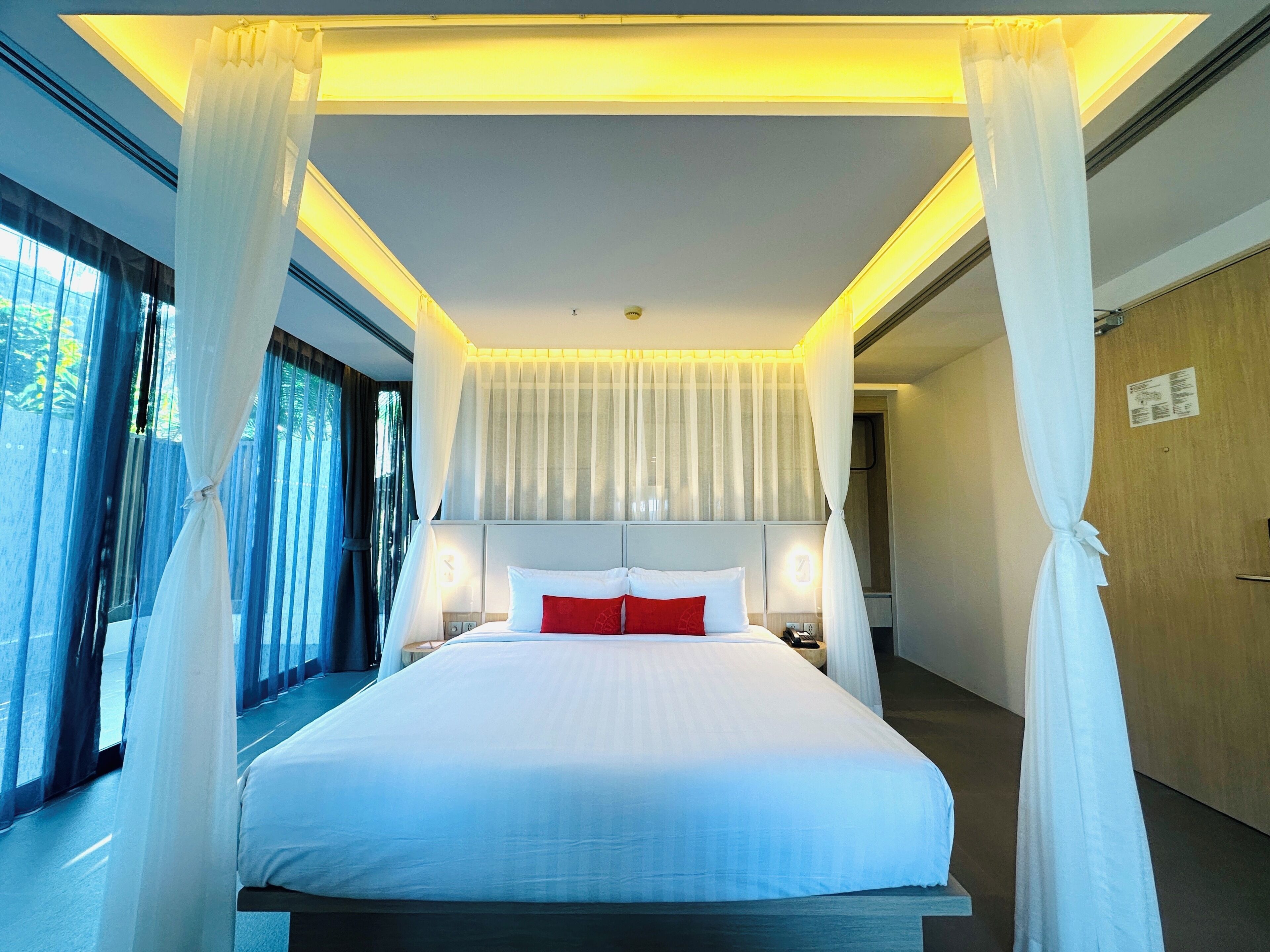 A hotel room with a large bed, white curtains, and a canopy.