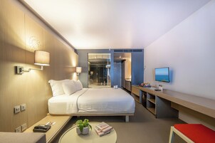 Habitación de hotel con cama, mesita de noche, lámpara, televisión y un pequeño escritorio.