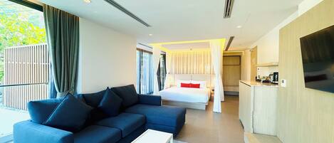 A modern hotel room with a sofa, a small white table, a bed with white bedding and red pillows, a TV, and a balcony with curtains.