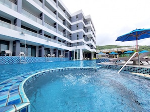 Relax by the pool with lounge chairs and umbrellas, surrounded by large windows and balconies.