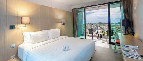 A hotel room with a large bed, a desk with a chair, and a balcony with a city view.
