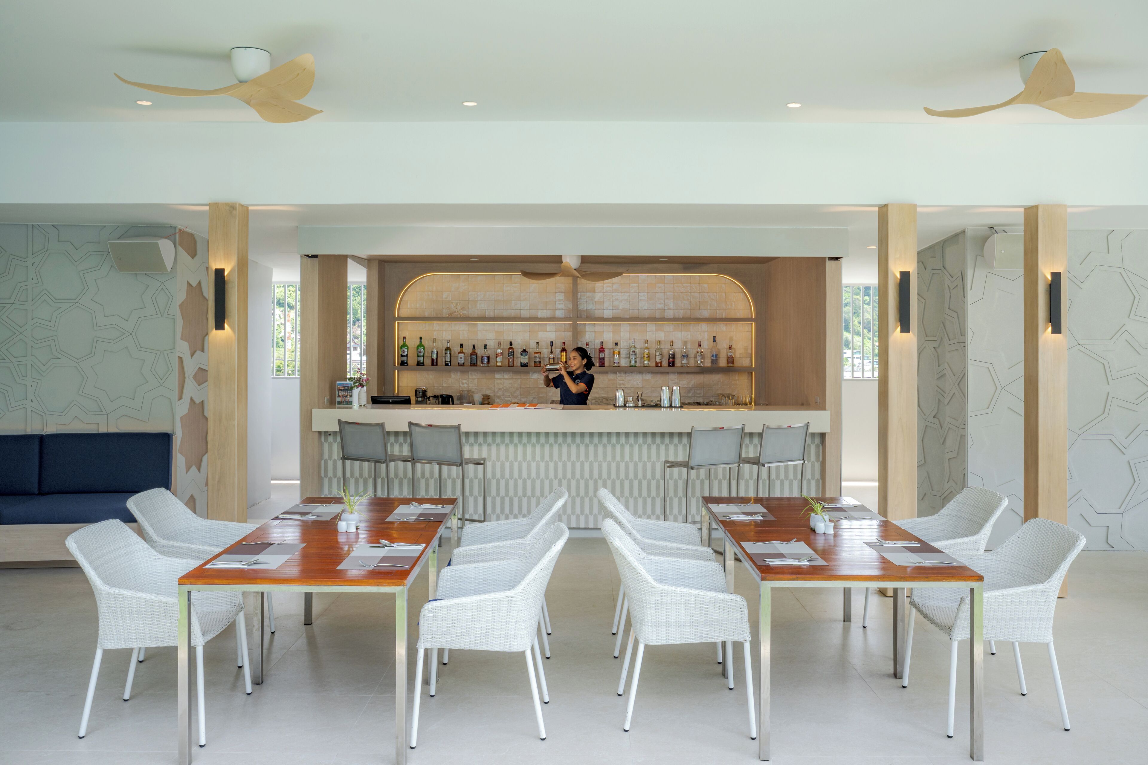 A modern bar area with a long counter, white wicker chairs, and a seating area with a sofa.