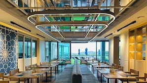 Un comedor moderno con un largo banco y varias mesas, ventanas amplias que ofrecen vistas al exterior, y un techo con un diseño geométrico único.