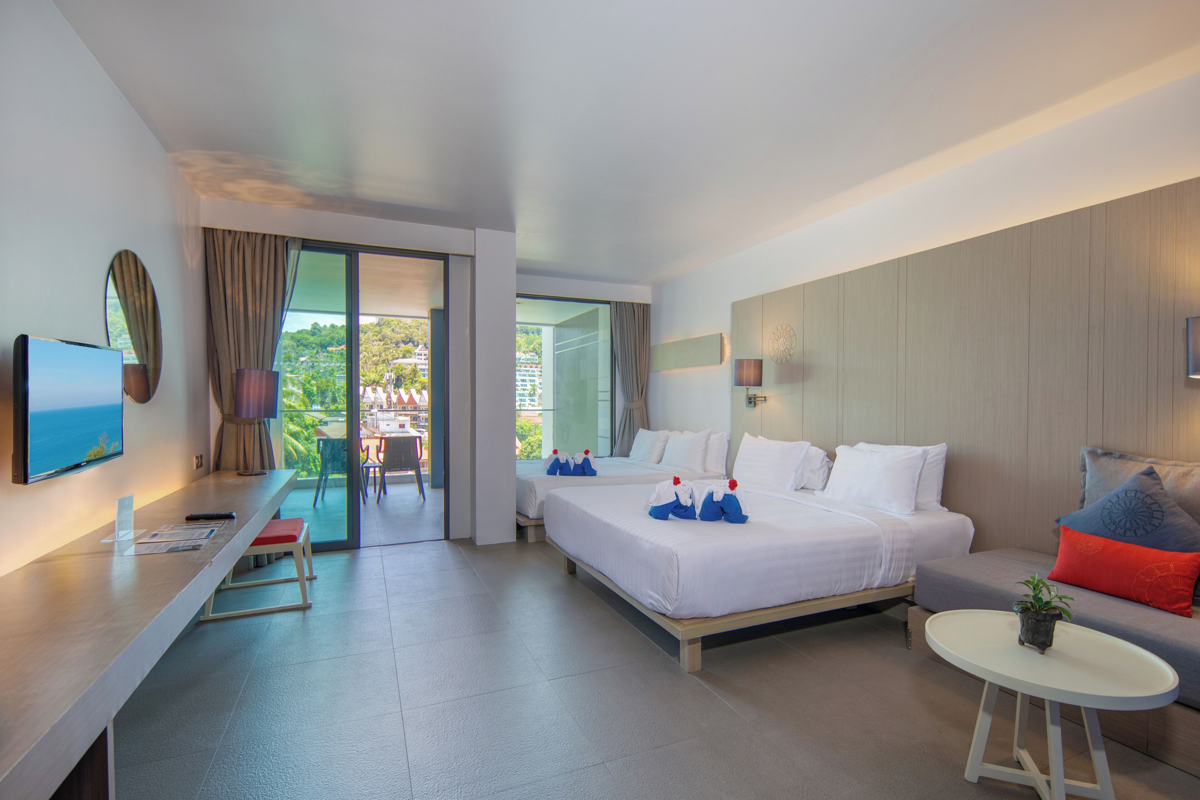 Una habitación de hotel moderna con una cama grande, un sofá, una mesita y un televisor.