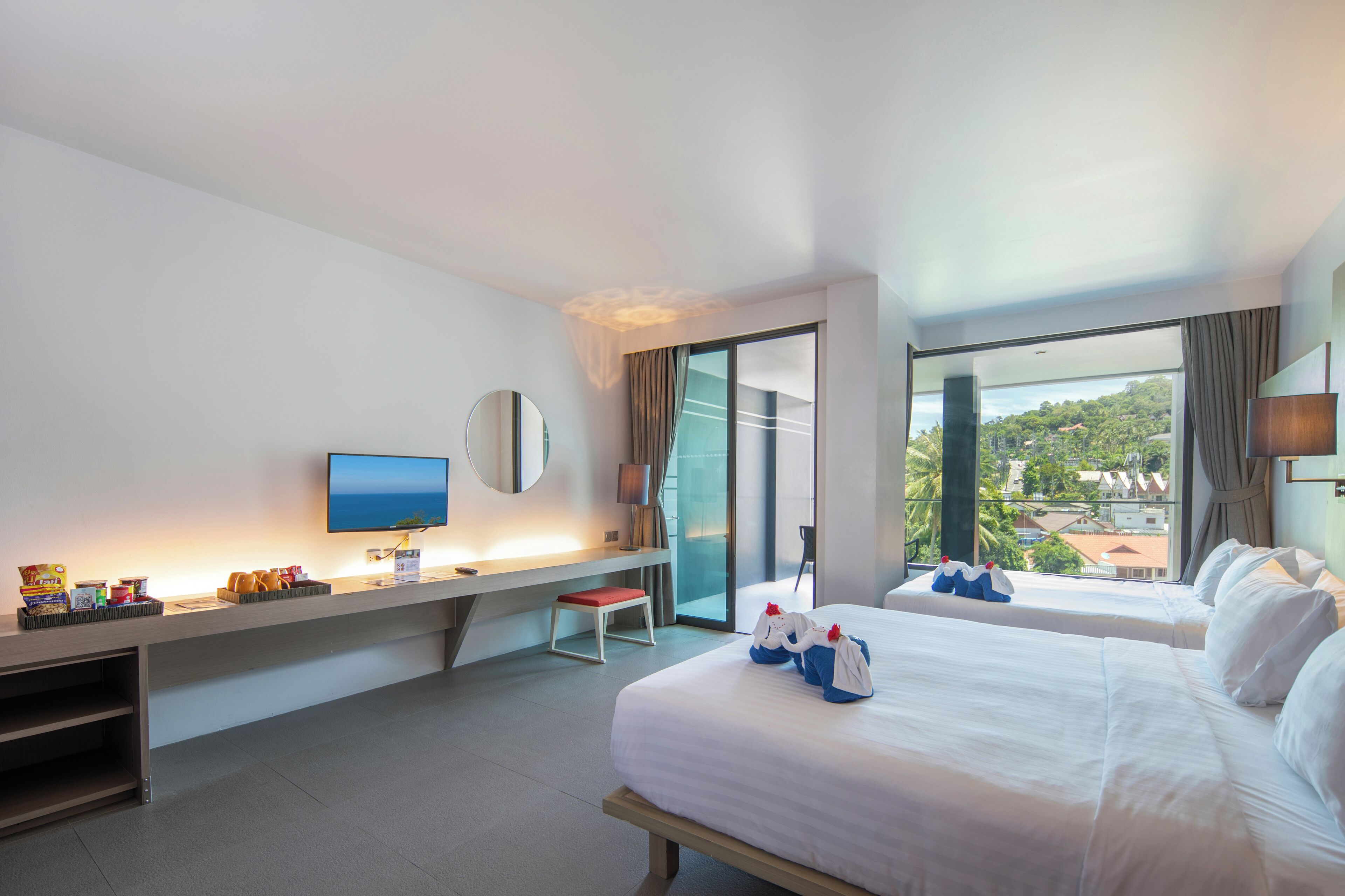 A hotel room with two beds, a desk with a computer, a TV, and a view of the outdoors.