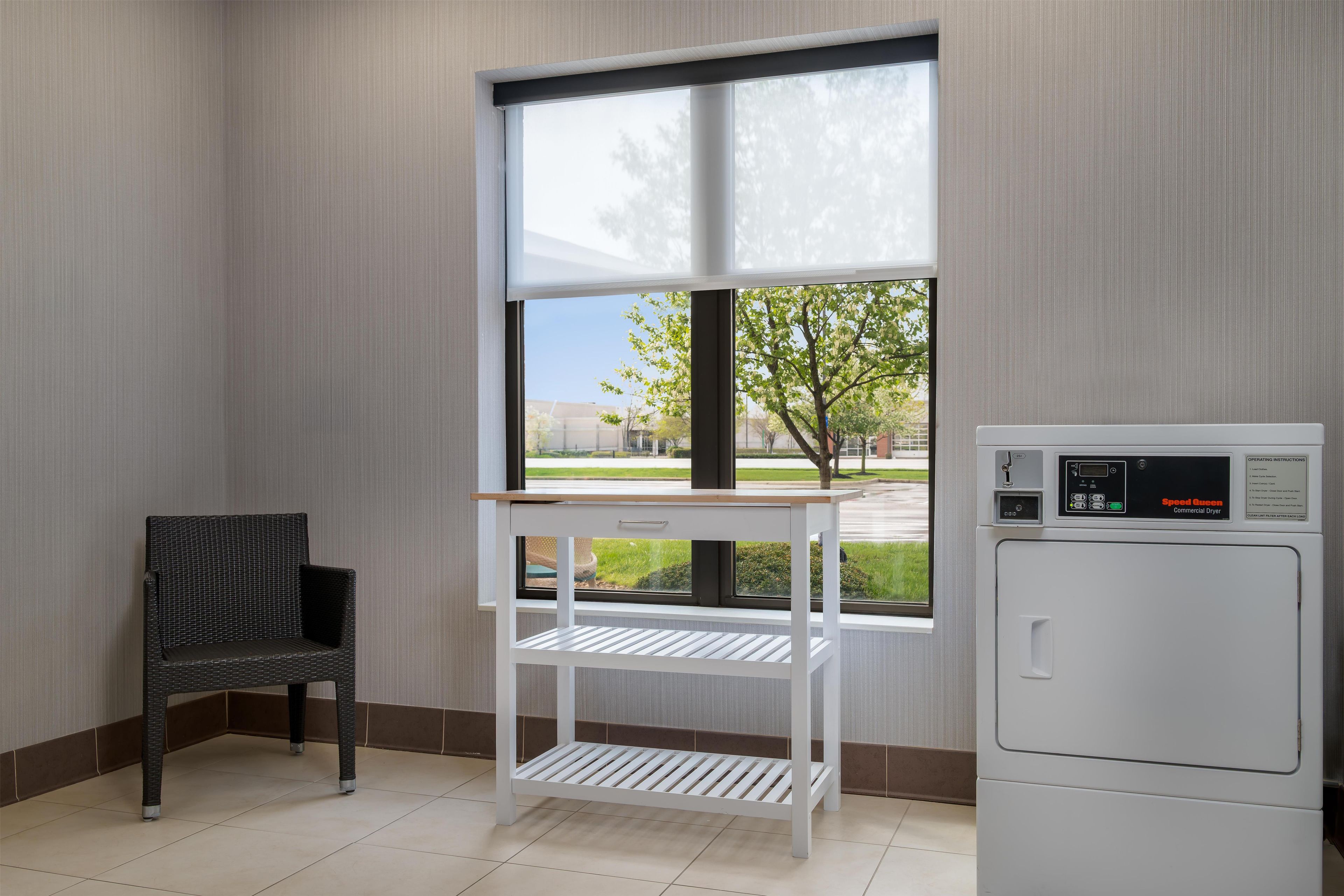 Una habitación con ventana, una silla y un secadora blanca.