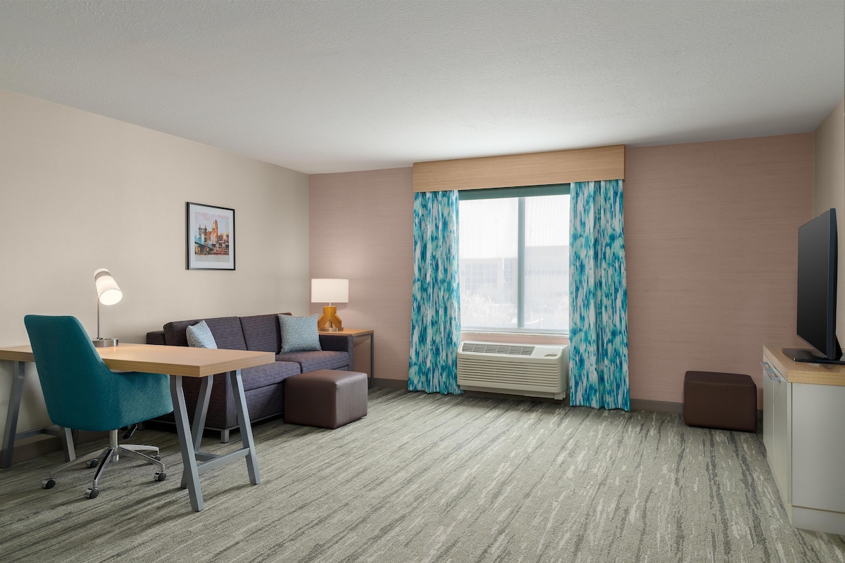 A hotel room with a desk, chair, sofa, and television.