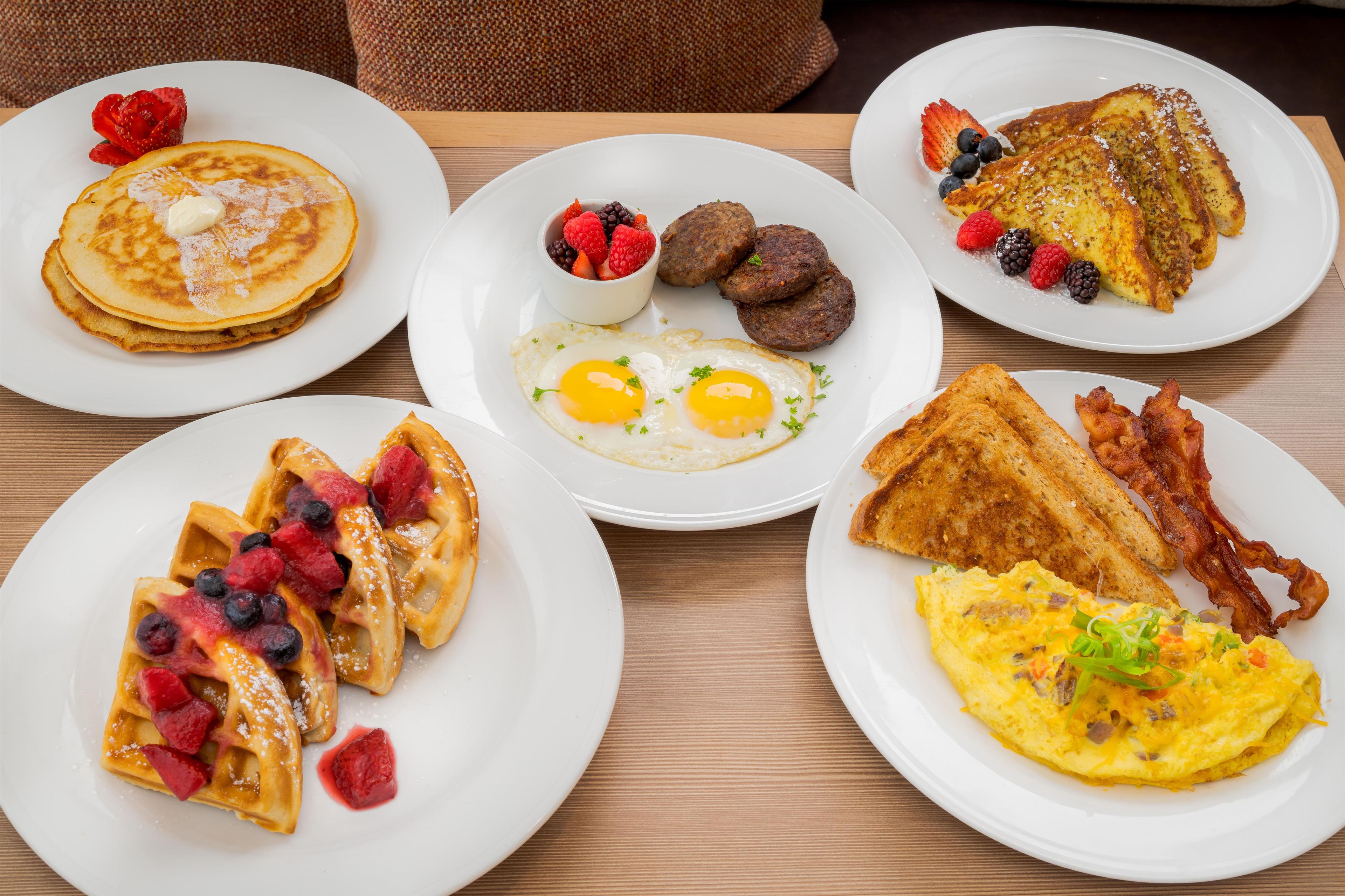 A breakfast spread with pancakes, waffles, eggs, toast, and bacon on white plates.