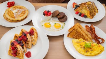 A breakfast spread with pancakes, waffles, eggs, toast, and bacon on white plates.