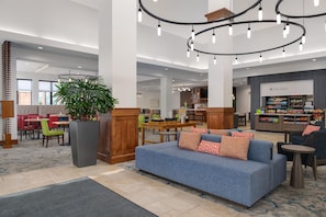 A spacious lobby with a blue sofa, a large plant, and a bar area.