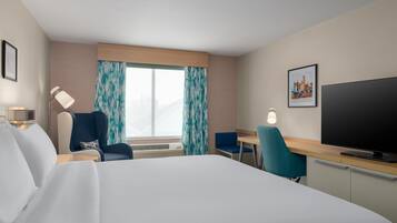 Quarto de hotel com cama, escrivaninha, cadeira, televisão e janela com cortinas.
