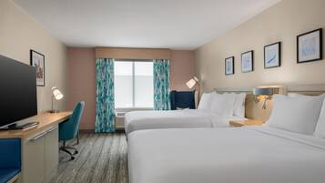 A hotel room with two beds, a desk, a chair, a TV, and a window with curtains.