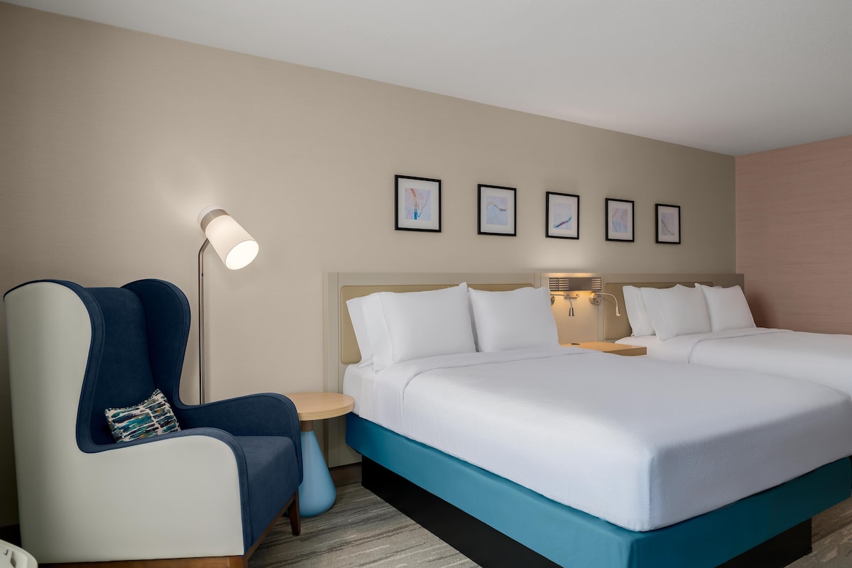 A hotel room with a bed, two bedside tables, a chair, a floor lamp, and four framed pictures on the wall.