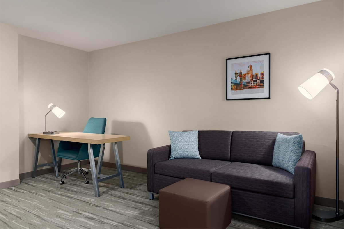 A room with a desk, chair, couch, ottoman, and two floor lamps.