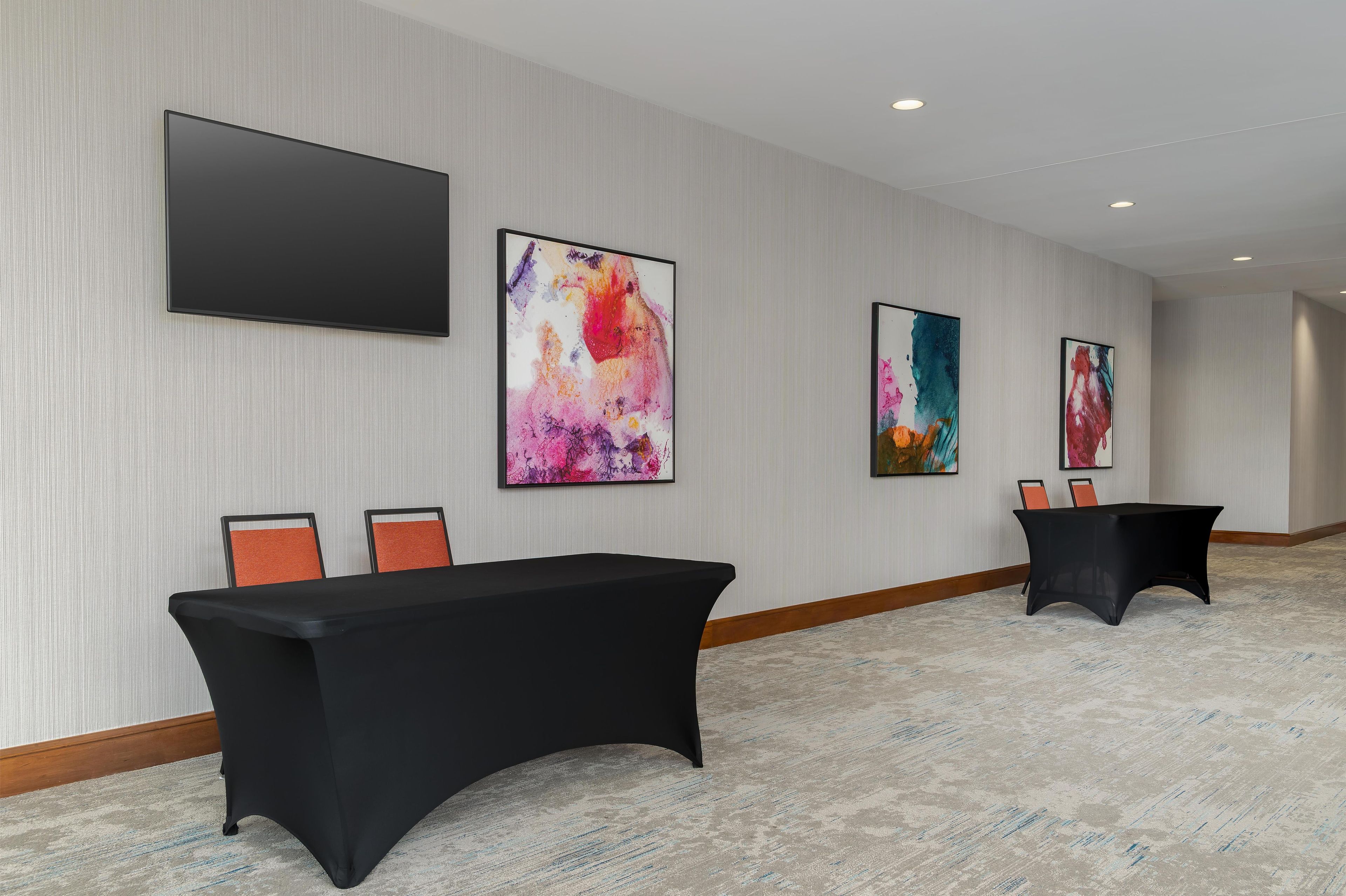 Une salle de conférence avec une longue table, deux chaises et trois tableaux abstraits accrochés au mur.