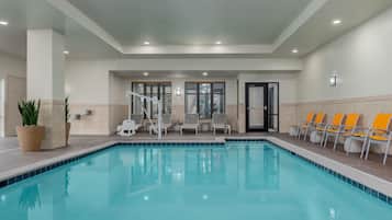 An indoor swimming pool with clear water, surrounded by lounge chairs and potted plants.