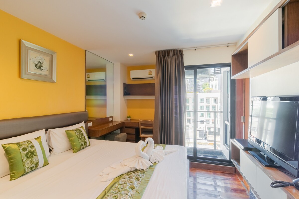 A hotel room with a bed, a desk, a television, and a large window.