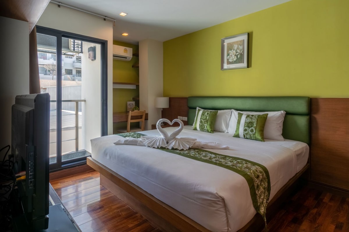 A hotel room with a large bed, a television, a green wall, and a picture of flowers.