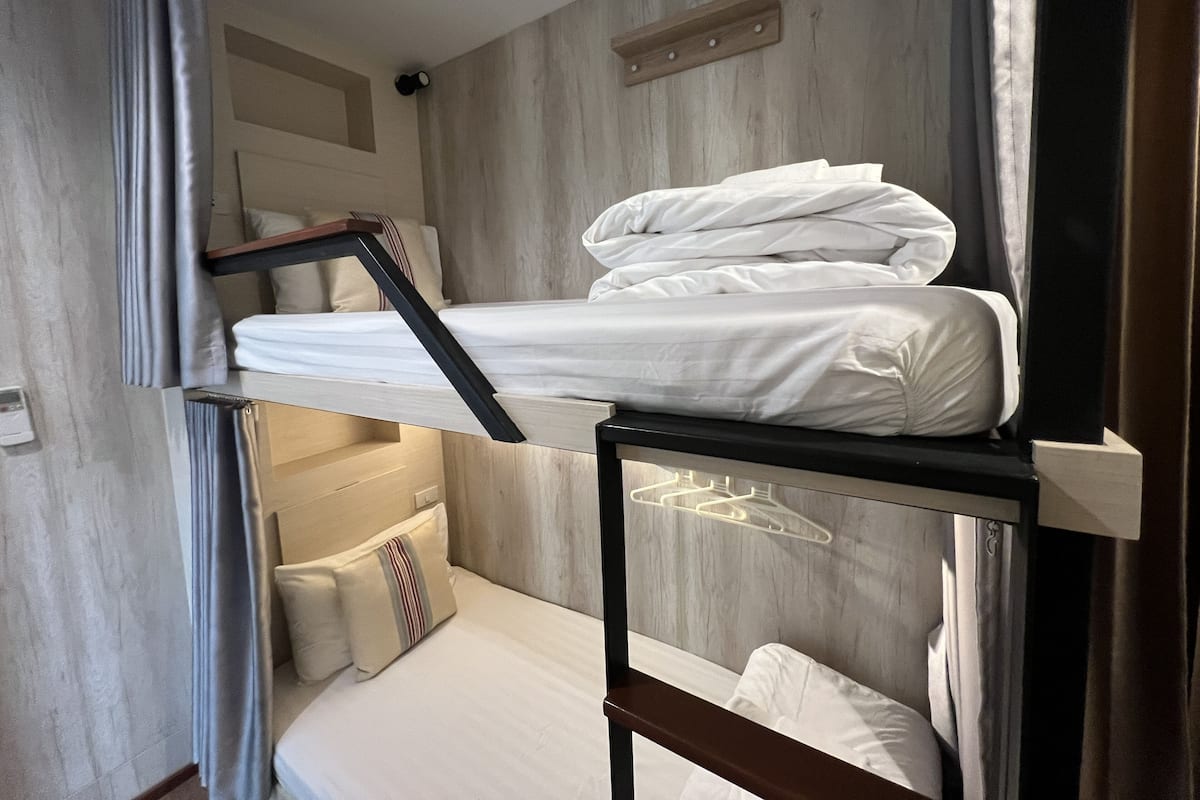 A bunk bed with white bedding, a wooden headboard, and a small bedside table with a lamp.