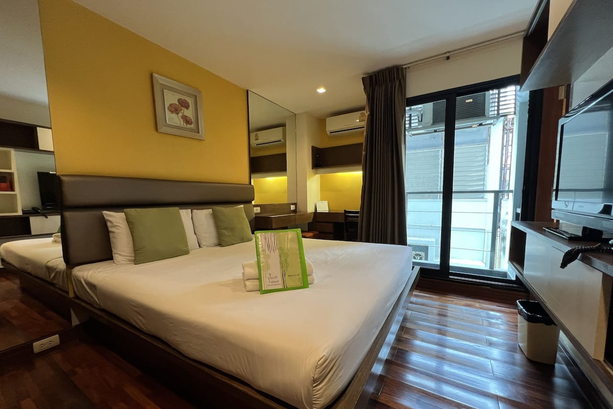 A hotel room with a large bed, a flat-screen TV, a desk, and a window with a view of the outside.