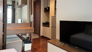 Une chambre d’hôtel moderne avec un plancher en bois, un téléviseur à écran plat, une petite kitchenette et une porte coulissante donnant sur la salle de bain.