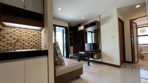 Une chambre d’hôtel moderne équipée d’une kitchenette, d’un canapé-lit, d’une télévision à écran plat et d’un grand miroir.