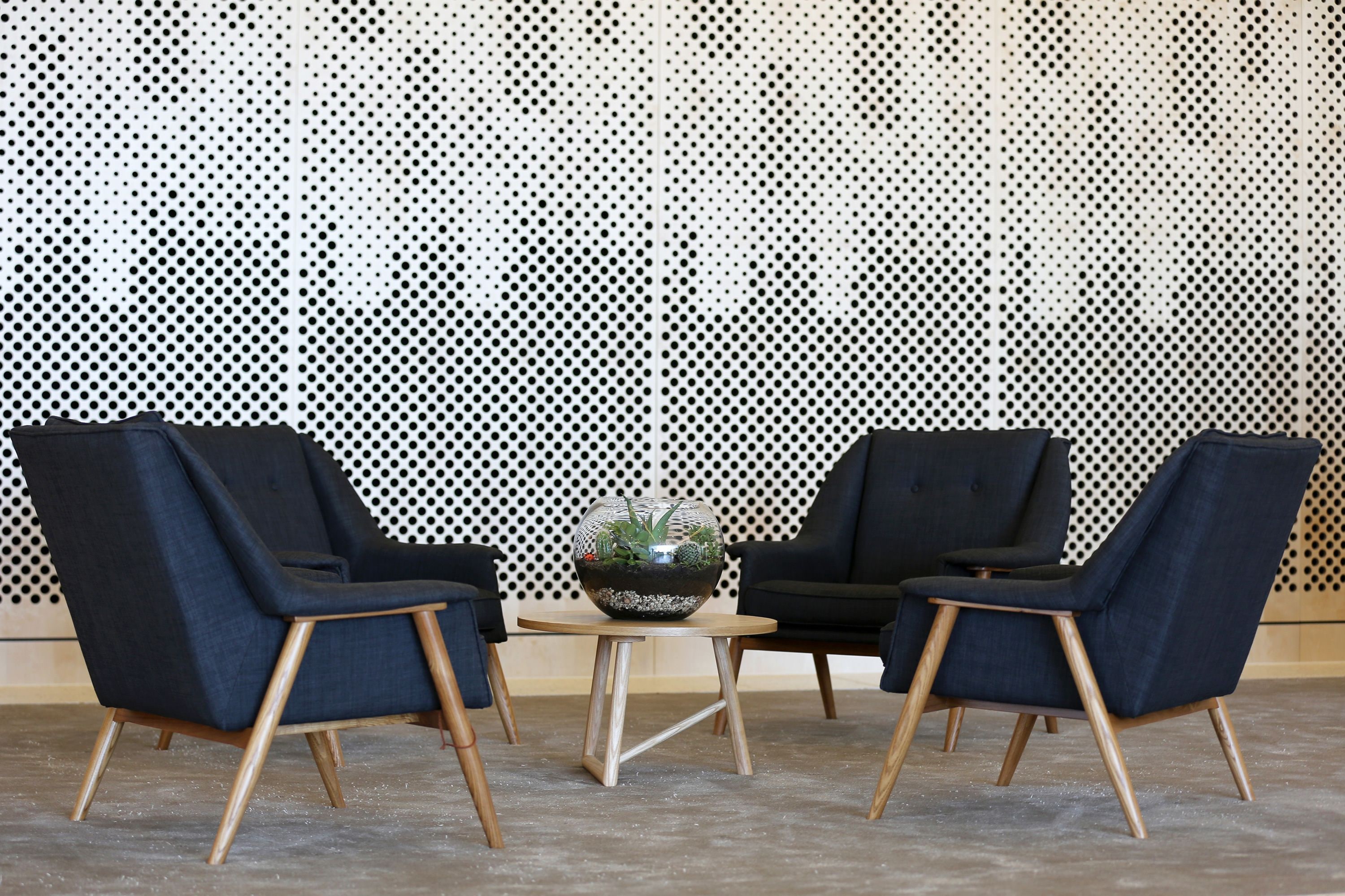 Une pièce avec deux fauteuils bleu foncé, une petite table ronde en bois et un bol en verre contenant une plante.