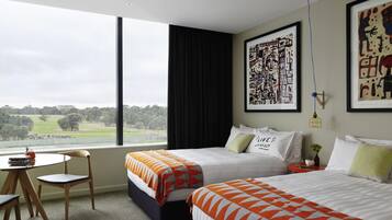 Een hotelkamer met twee bedden, een tafeltje, een stoel en een groot raam met uitzicht op het landschap.