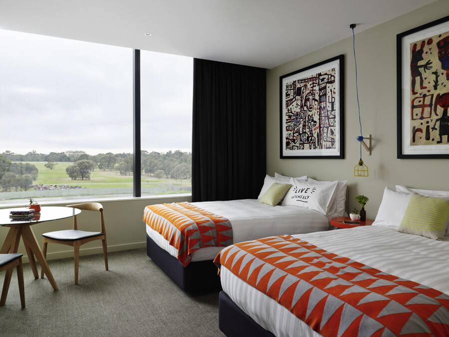 Een hotelkamer met twee bedden, een tafeltje, een stoel en een groot raam met uitzicht op het landschap.