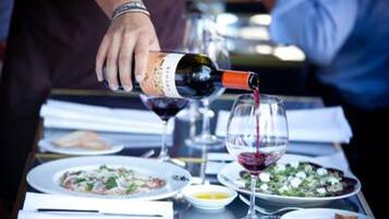 Una persona sirve vino en una copa sobre una mesa de comedor con varios platos y copas.