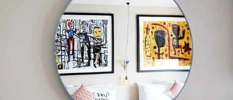 Ein Schlafzimmer mit einem Bett, zwei Kissen, einem Nachttisch und zwei gerahmten Kunstwerken an der Wand.
