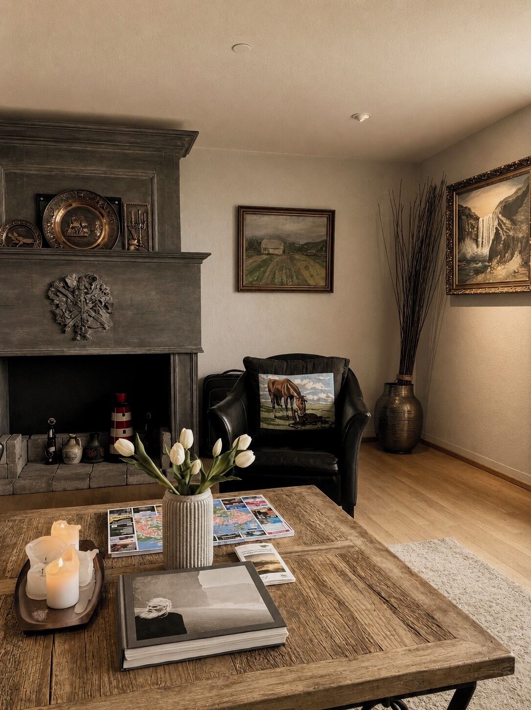 Un salon avec une cheminée, un fauteuil en cuir, une table basse avec des livres et un vase de fleurs, et une étagère au-dessus de la cheminée ornée d’objets décoratifs.