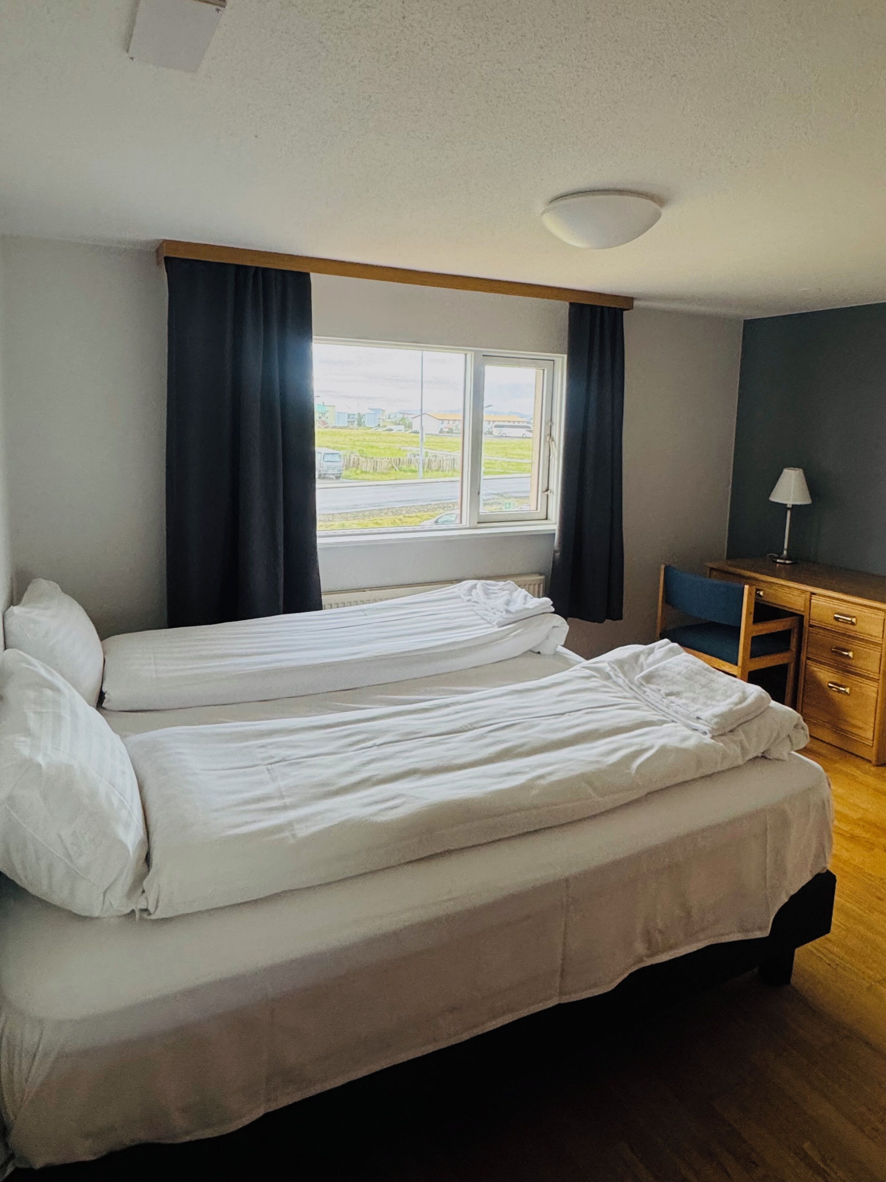 Habitación de hotel con dos camas, un escritorio, una silla y una ventana con vista al exterior.