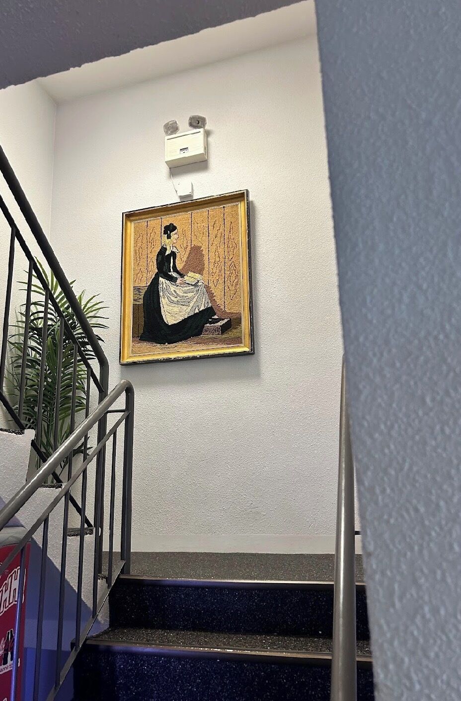 A staircase with a framed artwork on the wall, a metal handrail, and a potted plant.