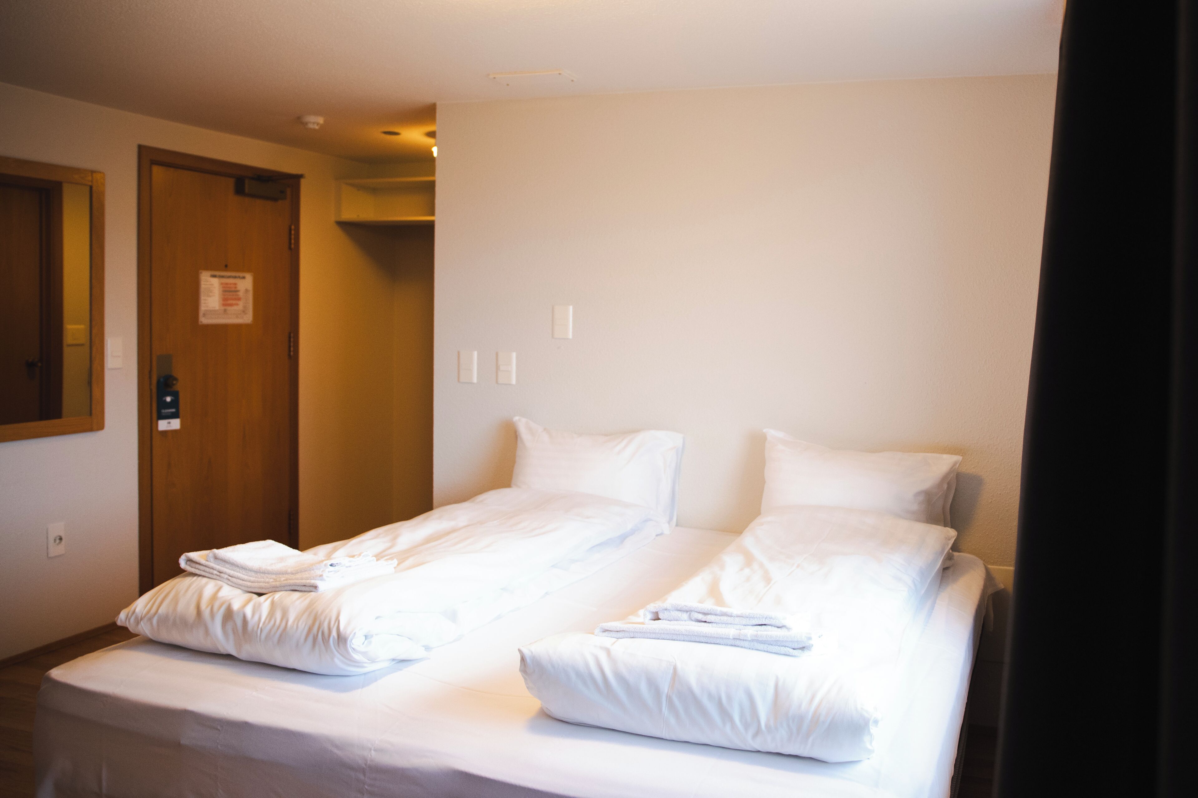 Una habitación de hotel con dos camas, una puerta de madera y un espejo en la pared.