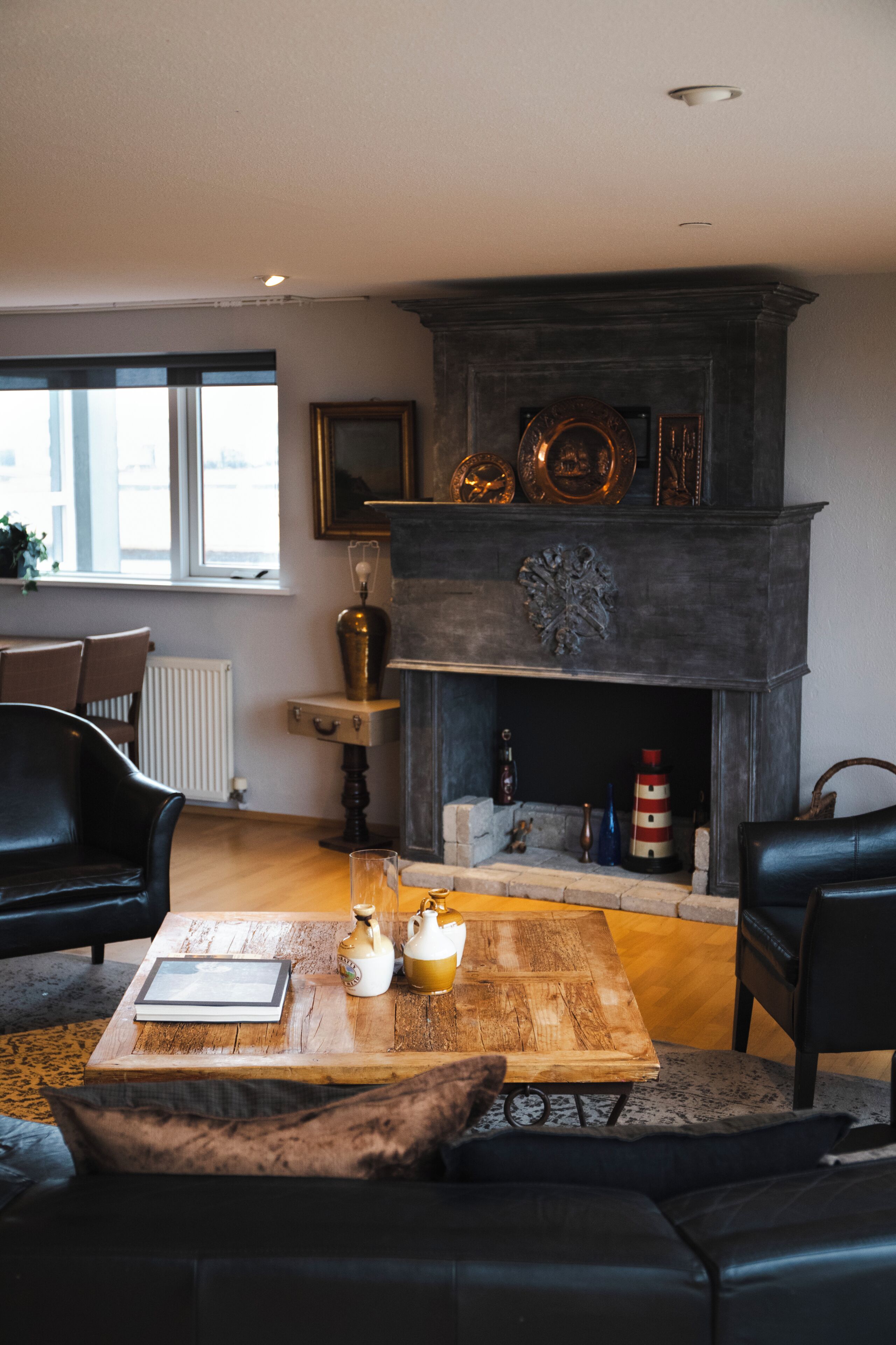 Un salón con chimenea, sofás de cuero, una mesa de centro con libros y objetos decorativos, y un ventanal que proporciona luz natural.