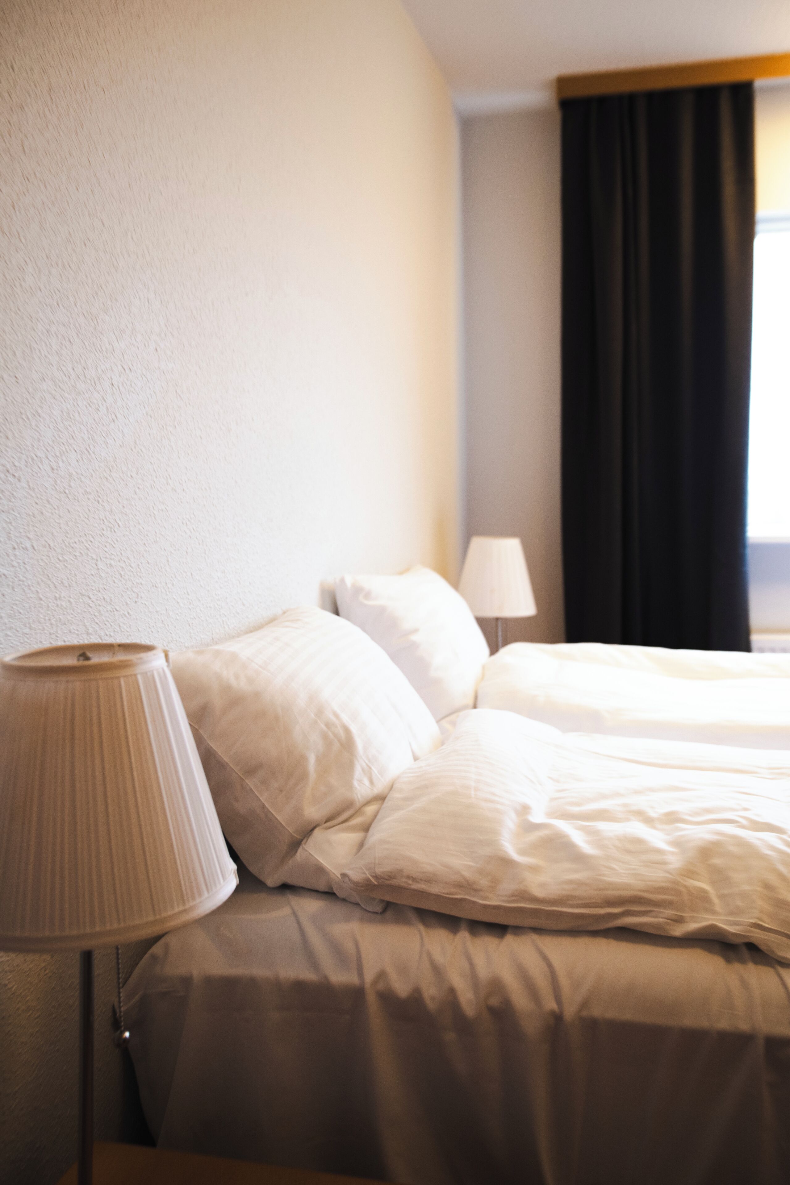 A hotel room with a bed, a lamp, and a window with curtains.