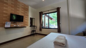 Ein Hotelzimmer mit einem Bett, einem an einer Ziegelwand montierten Fernseher, einem Fenster mit Vorhängen und einem Sessel.