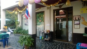 A restaurant with outdoor seating, a flag, and a sign for Phumthong Homestay. - Phurahong Homestay (Bangkok)