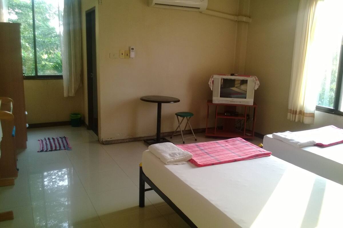 A hotel room with a bed, a small table, a TV on a stand, and a window with curtains.
