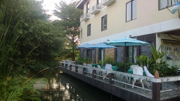 A riverside restaurant with outdoor seating and a stone wall backdrop. - Phurahong Homestay (Bangkok)