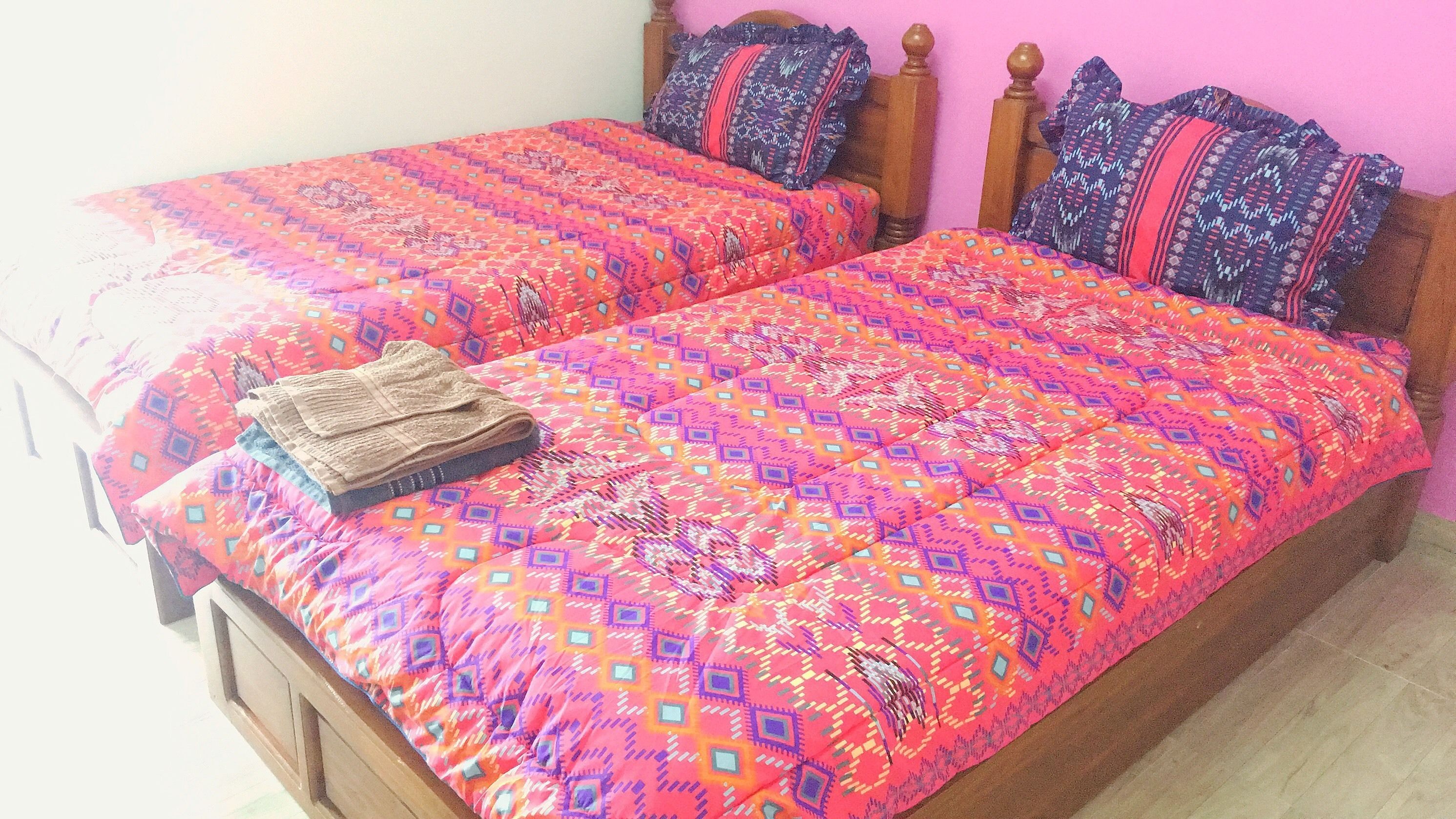 Una cama doble con un edredón estampado y colorido y dos almohadas, un cabecero de madera y una mesita de noche con una lámpara.