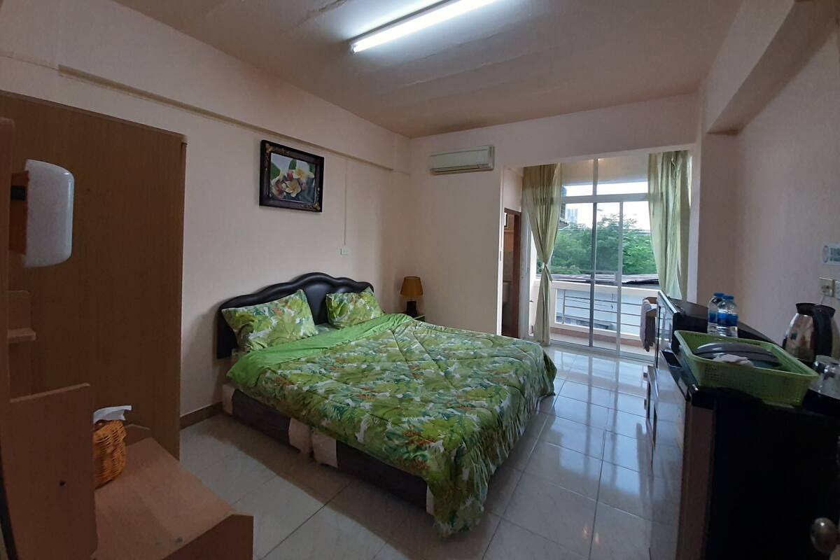 A hotel room with a bed, a desk, a chair, a window with curtains, and a door.